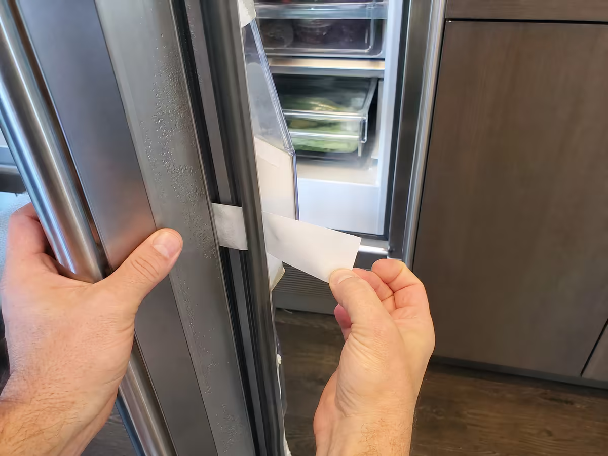 Hand pointing to a Sub-Zero model and serial tag on the upper interior wall of the fresh-food compartment